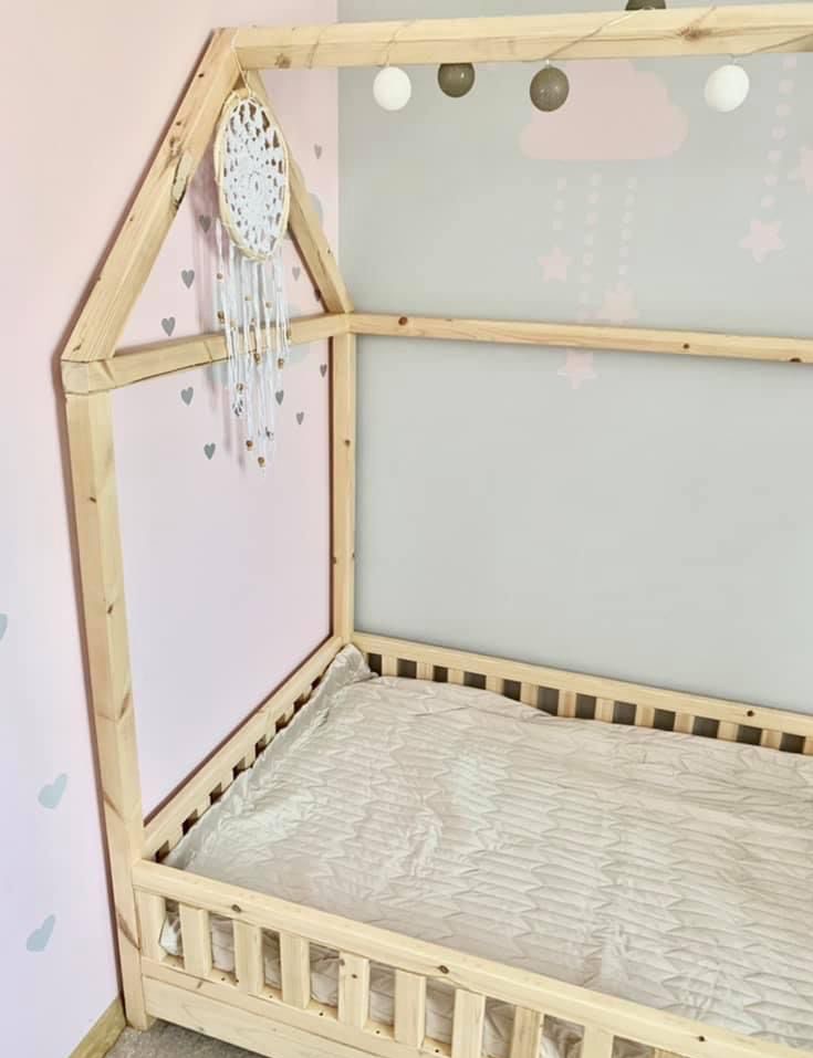 Drewniane łóżko domek dla dziecka z dekoracjami: łapacz snów i lampki cotton balls. Pastelowe ściany w serduszka i chmurki. Jasne drewno, naturalny styl.