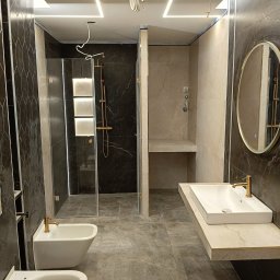 BUD-MAR - Nowoczesna łazienka z kabiną prysznicową typu walk-in, umywalką na blacie i podświetleniem LED. Ciemne płytki imitujące marmur. Wnętrze w trakcie wykańczania.