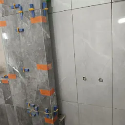 Montaż płytek imitujących marmur na ścianie z użyciem poziomicy laserowej i klipsów poziomujących. Widoczne otwory na gniazdka.