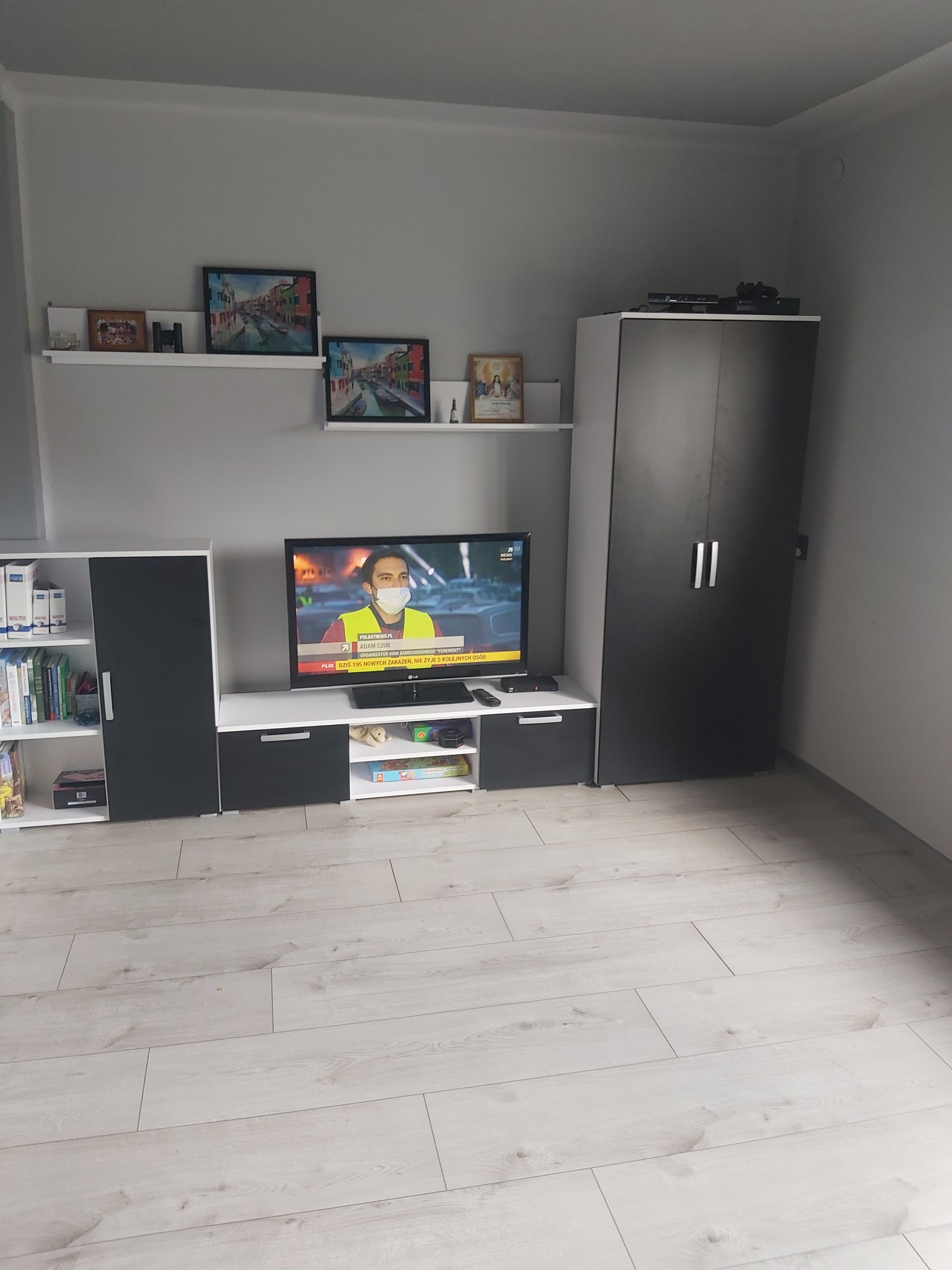 Nowoczesny salon w odcieniach szarości i bieli. Meble w zabudowie, telewizor, dekoracje ścienne. Jasna podłoga z paneli. Minimalistyczny design.