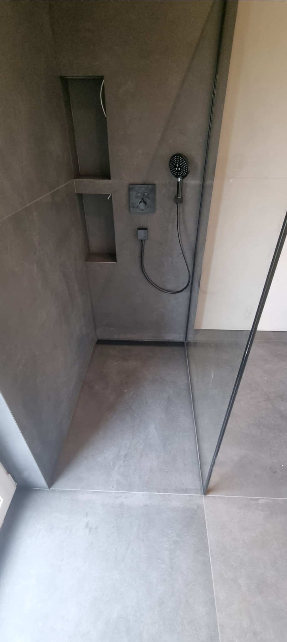 Szara kabina prysznicowa walk-in z wnękami w ścianie na kosmetyki i czarną armaturą. Minimalistyczny design, nowoczesne wykończenie.