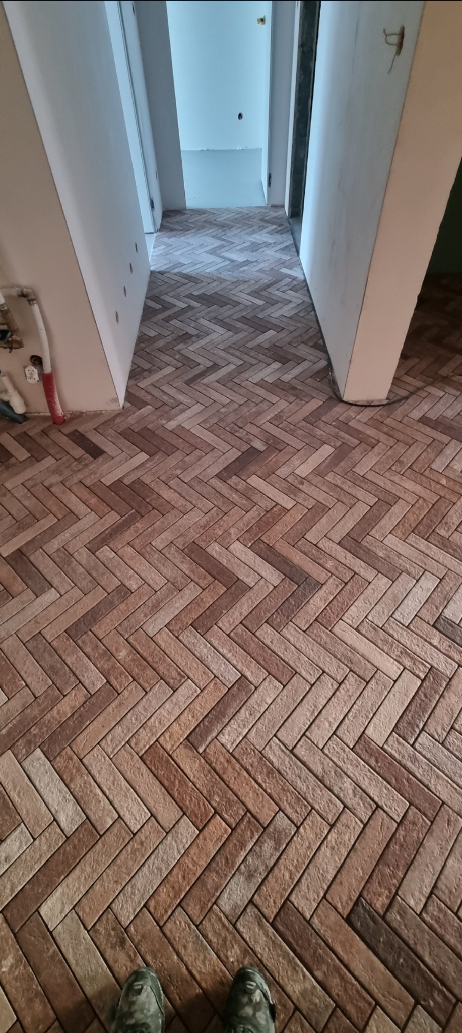 Ukończona podłoga z brązowych płytek ułożonych w jodełkę, widok z perspektywy osoby stojącej na niej. Białe filary po bokach, dalsza część korytarza w tle.