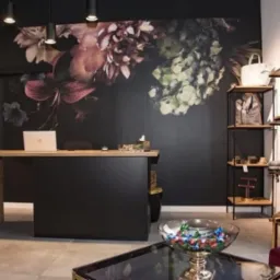 Nowoczesne biuro z recepcją, czarne ściany zdobione kwiatowym motywem, drewniany blat, metalowy regał i szklany stolik kawowy z dekoracjami.