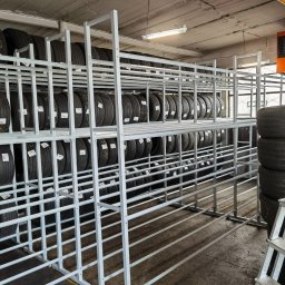 Rafał Adamczuk ALLStal - Metalowa konstrukcja regału na opony w warsztacie. Widoczne opony z etykietami, drabina aluminiowa. Szara podłoga i sufit z oświetleniem.