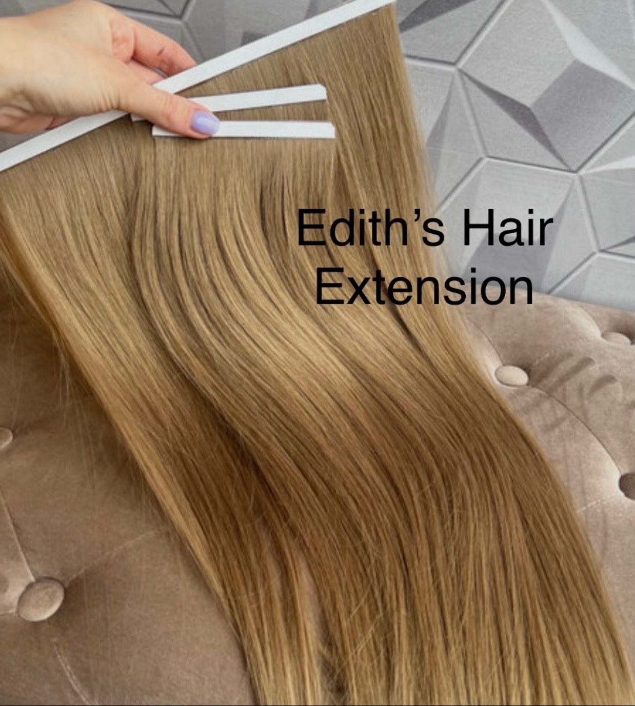 Blond doczepy włosów tape-on prezentowane na tle wzorzystej ściany i pluszowego mebla. Widoczne taśmy mocujące i dłoń z delikatnym manicure.