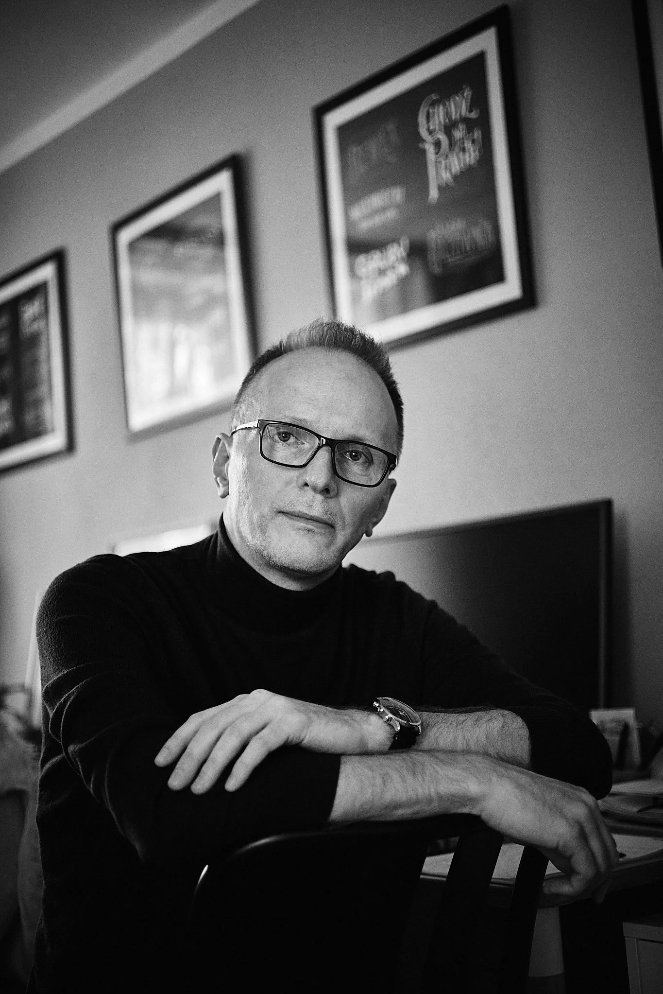 Czarno-biały portret biznesowy mężczyzny w okularach, siedzącego na krześle z założonymi rękami, w tle obrazy na ścianie, Warszawa.