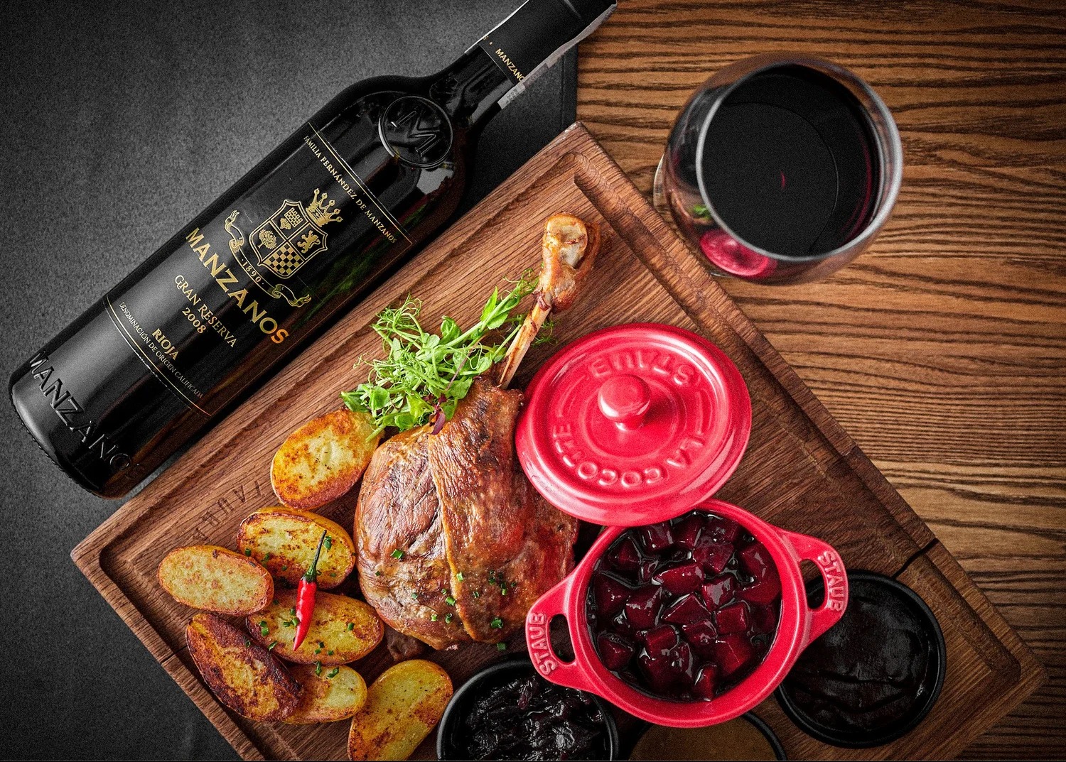 Elegancka kompozycja kulinarna: kaczka, ziemniaki z papryczką chili, buraczki w czerwonym naczyniu Staub, sosy i butelka wina Manzanos Gran Reserva Rioja 2008.