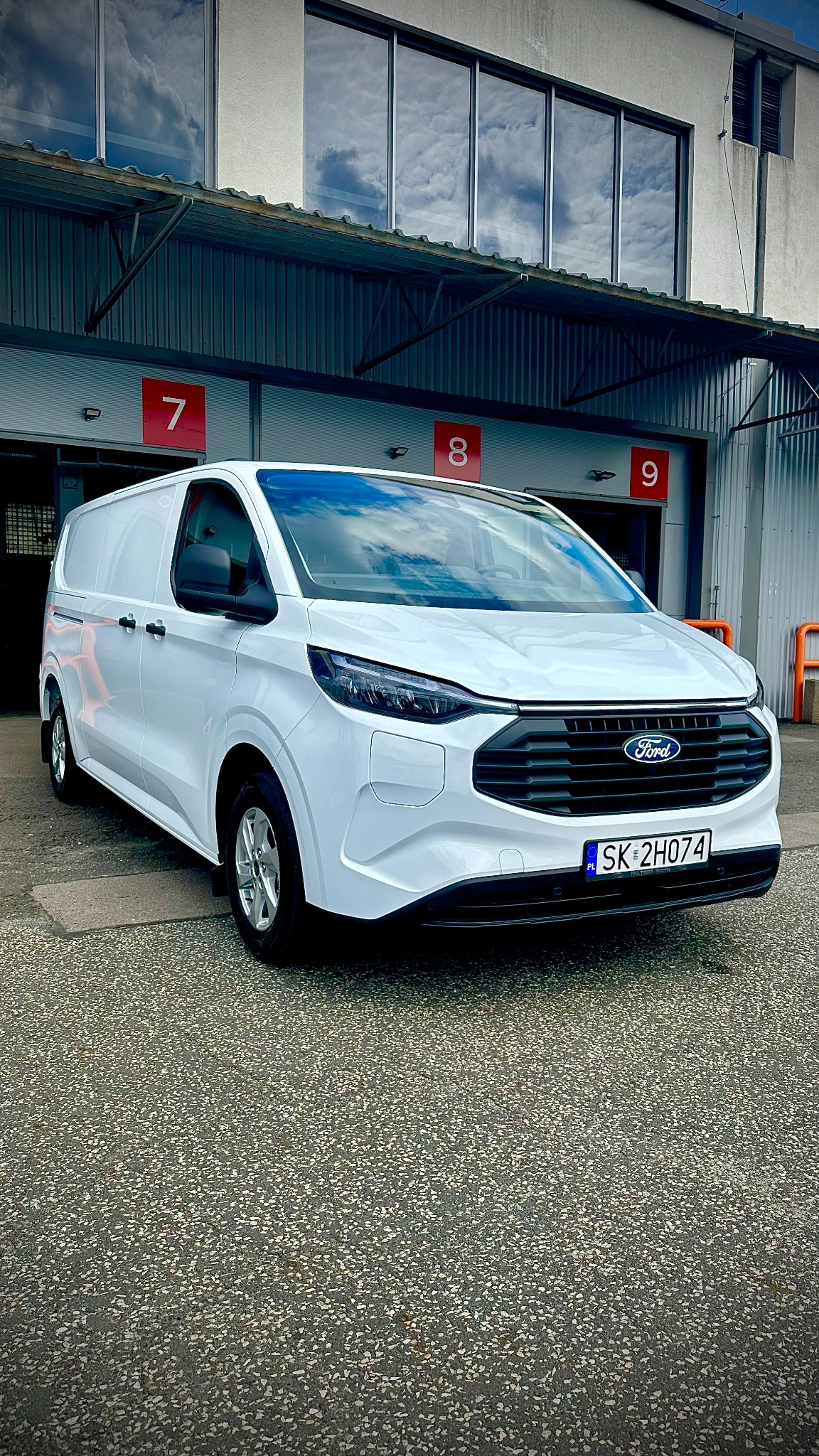 Biały, nowoczesny Ford Transit Custom, z widoczną tablicą rejestracyjną SK 2H074, zaparkowany przed budynkiem z numerami 7, 8 i 9.
