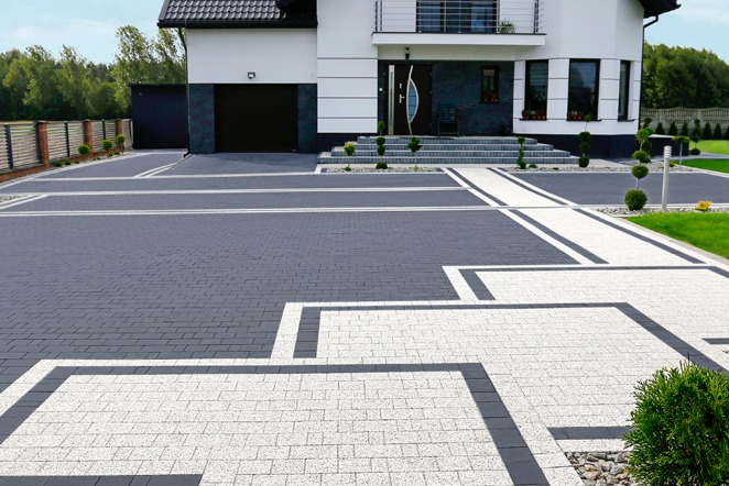 Dwukolorowa kostka brukowa ułożona we wzór geometryczny przed nowoczesnym domem z garażem. Widoczne schody wejściowe i zadbana zieleń.