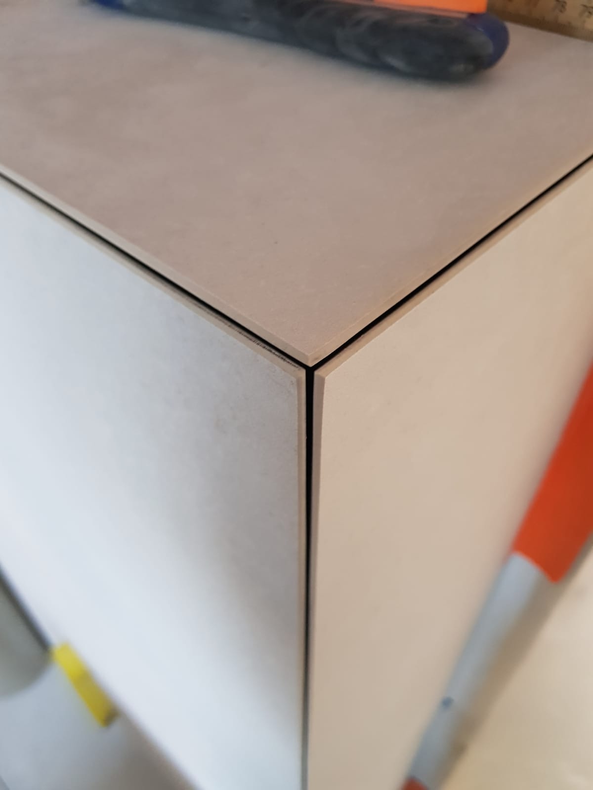 Precyzyjnie ułożone, jasne płytki narożne z wąską fugą, na blacie widoczny nóż do cięcia płytek. Detal wykończenia łazienki.