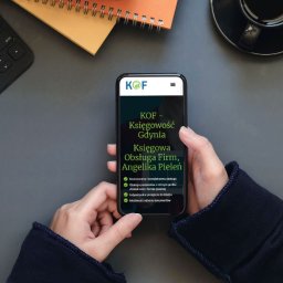 R4BL Media Radosław Barański - Telefon w dłoniach wyświetla stronę KOF Księgowość Gdynia, prezentującą ofertę obsługi księgowej dla firm. Widoczny notatnik, klawiatura i filiżanka kawy w tle.