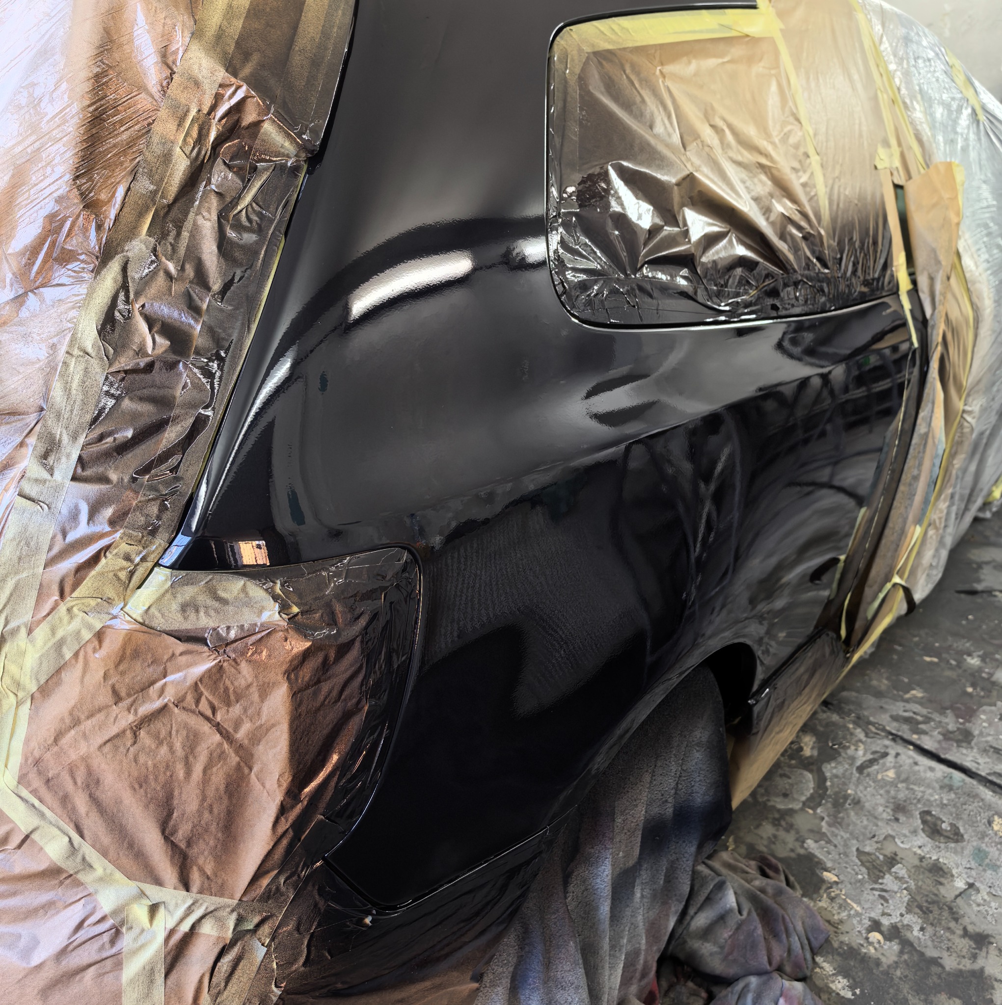 Częściowo oklejony samochód po lakierowaniu; widoczne elementy karoserii w czarnym, błyszczącym lakierze, przygotowane do dalszych prac wykończeniowych.