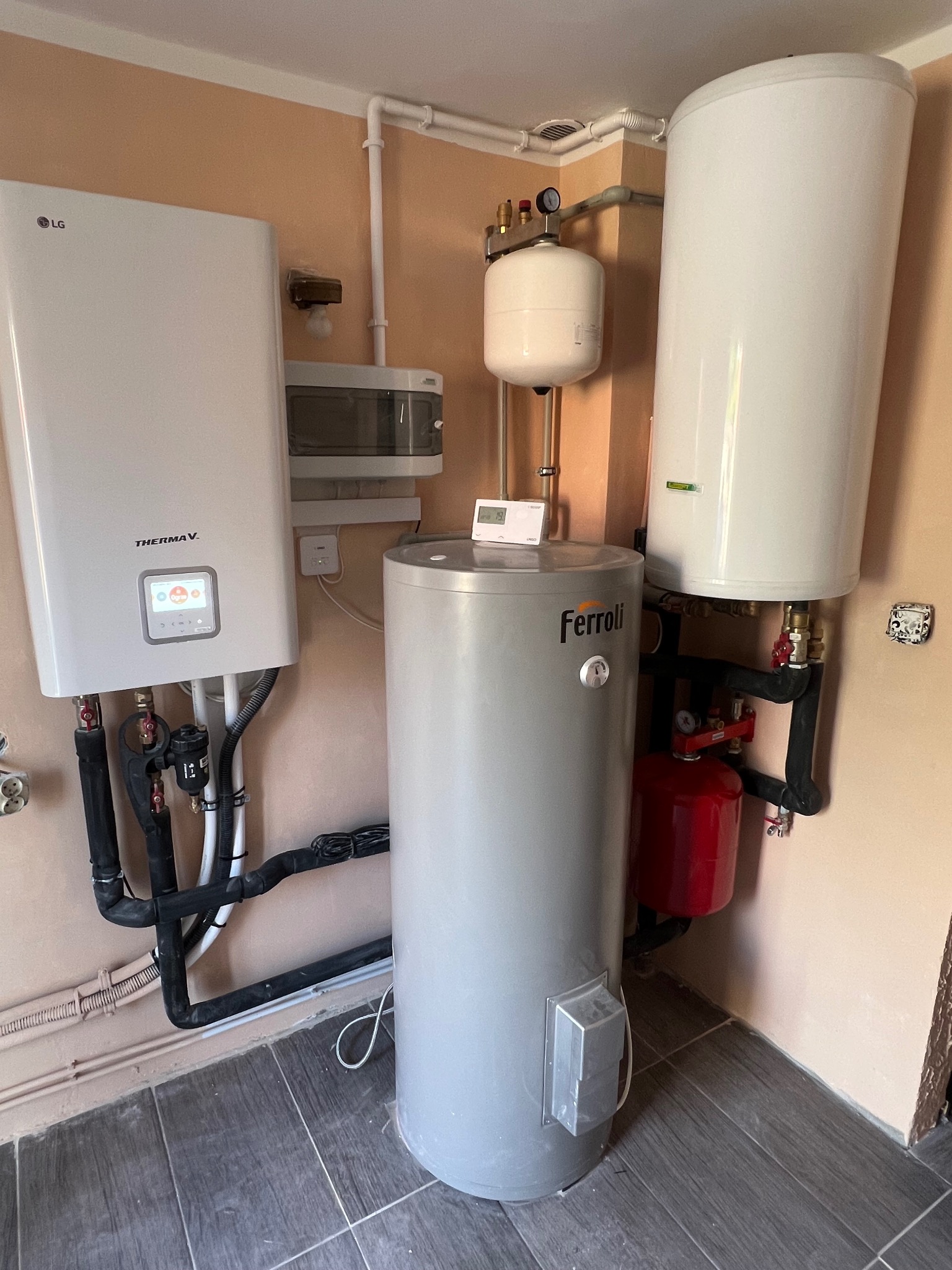 Zestaw urządzeń grzewczych: pompa ciepła LG Therma V, zbiornik Ferroli, naczynia przeponowe i rury. Kompaktowa instalacja w pomieszczeniu technicznym.