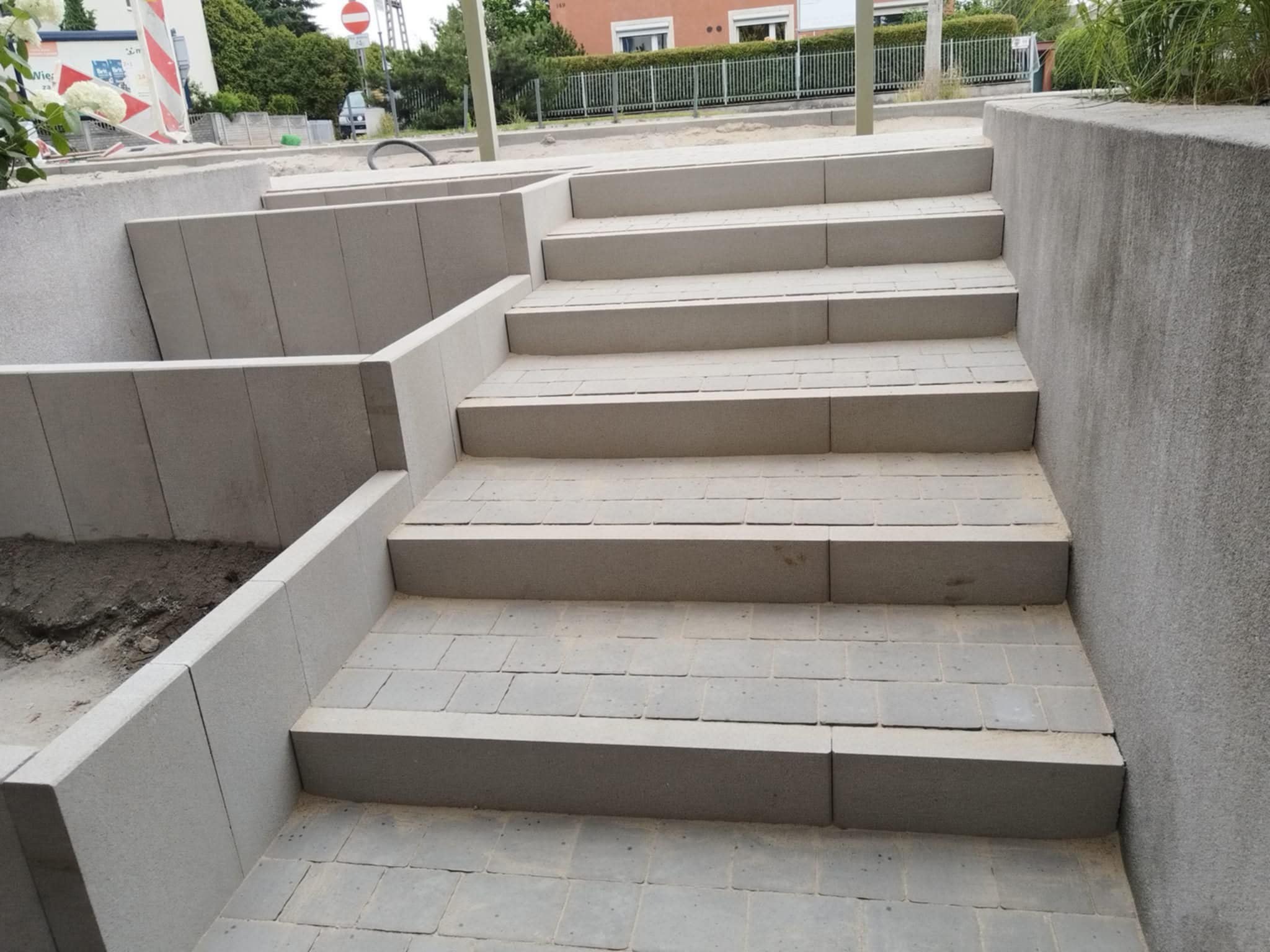 Schody z kostki brukowej w szarej tonacji, z widocznymi betonowymi ściankami bocznymi, prowadzące w górę. Ujęcie z dołu, podkreślające perspektywę.