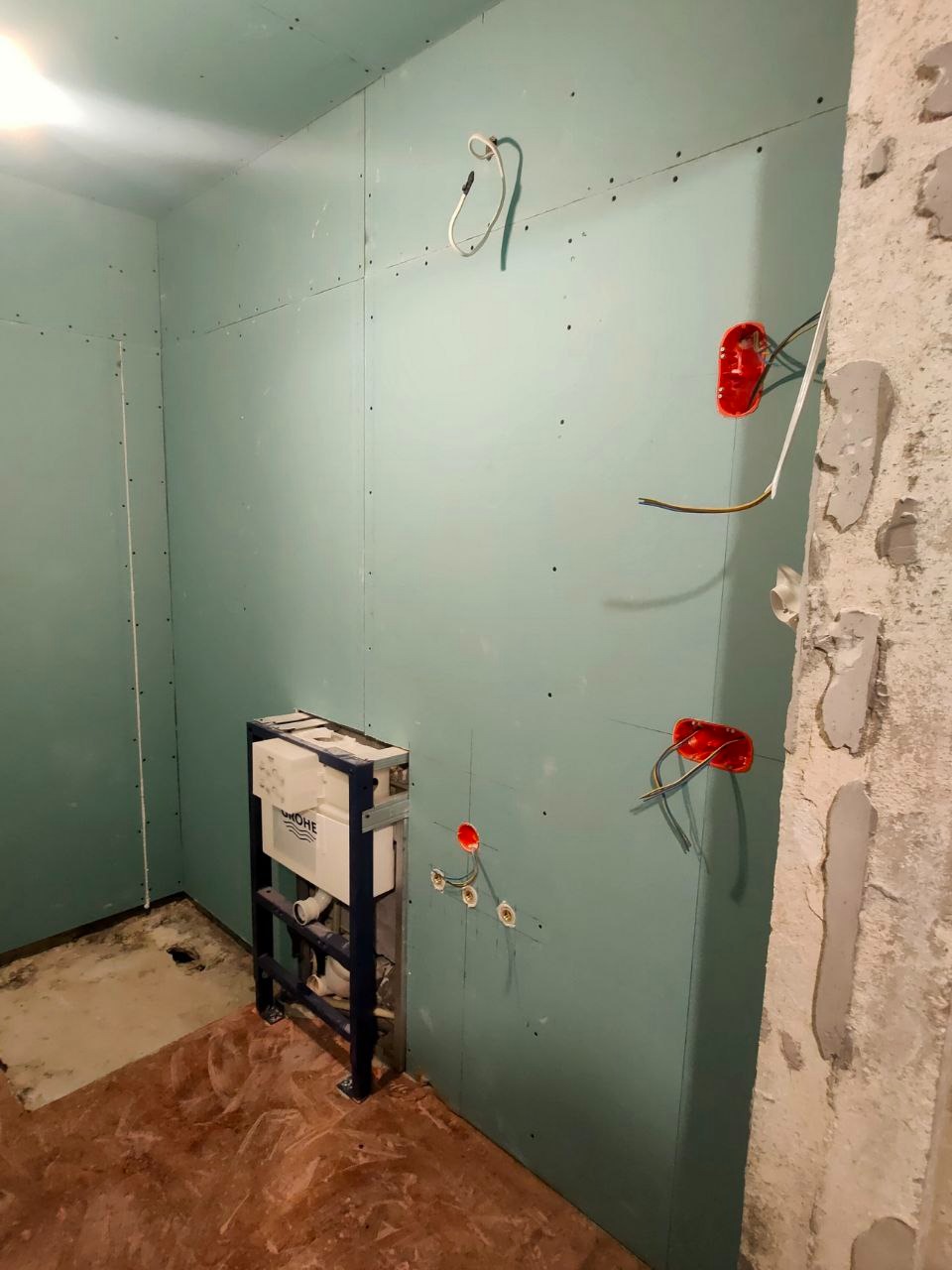 Łazienka w trakcie prac: zamontowany stelaż podtynkowy WC, płyty GK na ścianach, instalacja elektryczna w puszkach. Surowy stan, przygotowanie do dalszych prac wykończeniowych.