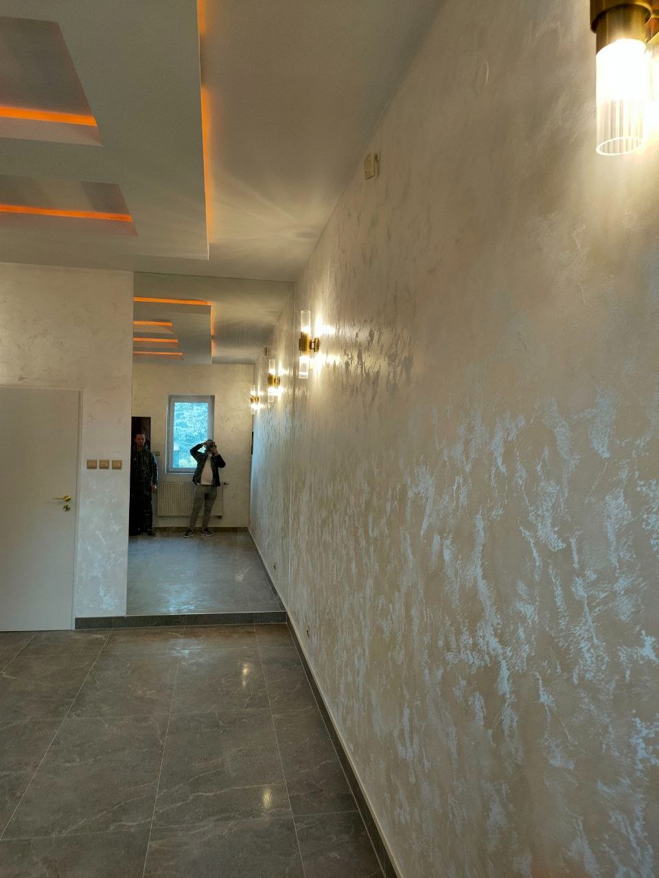 Eleganckie wykończenie wnętrza: ściana z efektem dekoracyjnym, podłoga z płytek imitujących marmur, subtelne oświetlenie LED i lustra optycznie powiększające przestrzeń.