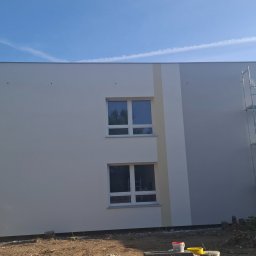 Serhii Kupriianchuk - Dwukondygnacyjny budynek po malowaniu elewacji w odcieniach bieli i szarości, z widocznymi rusztowaniami i dwoma oknami na każdej kondygnacji.
