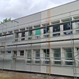 Serhii Kupriianchuk - Budynek po renowacji elewacji, z widocznymi rusztowaniami i fragmentem zieleni. Jasna kolorystyka budynku z akcentami w odcieniach szarości i beżu.