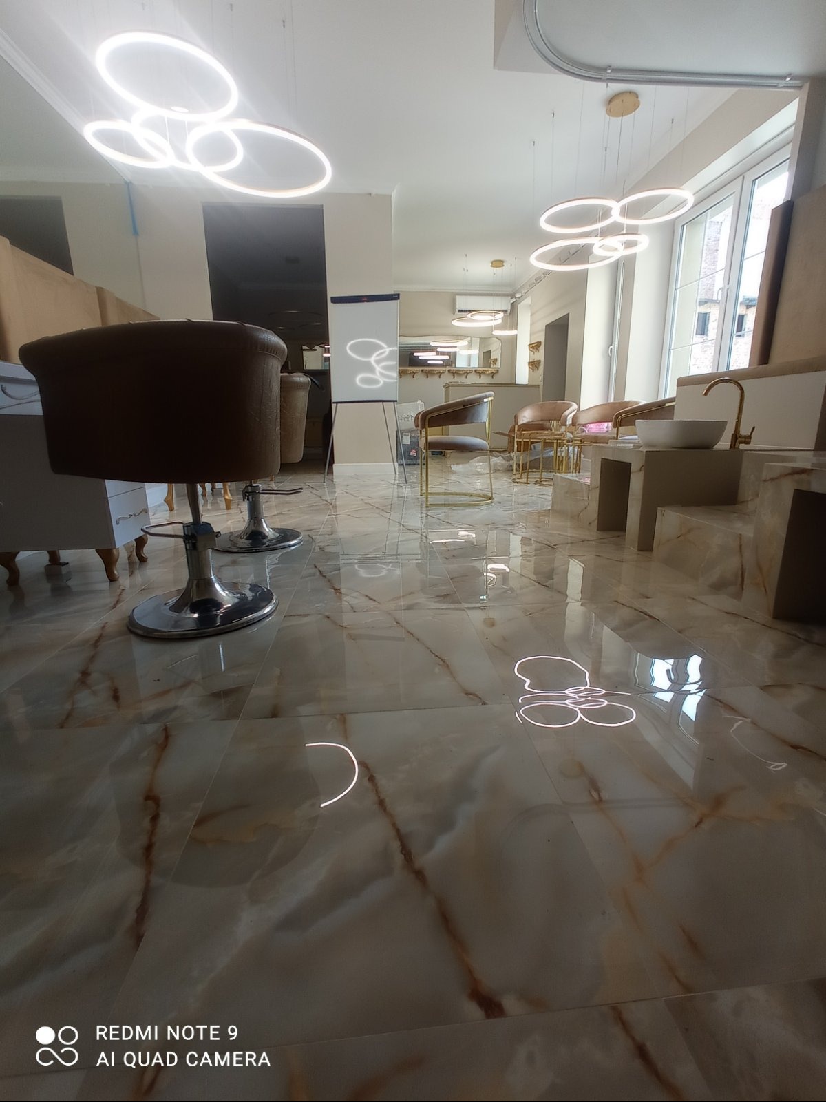 Błyszcząca, marmurkowa podłoga w salonie kosmetycznym z krzesłami, umywalką i dekoracyjnym oświetleniem. Widok z niskiej perspektywy.