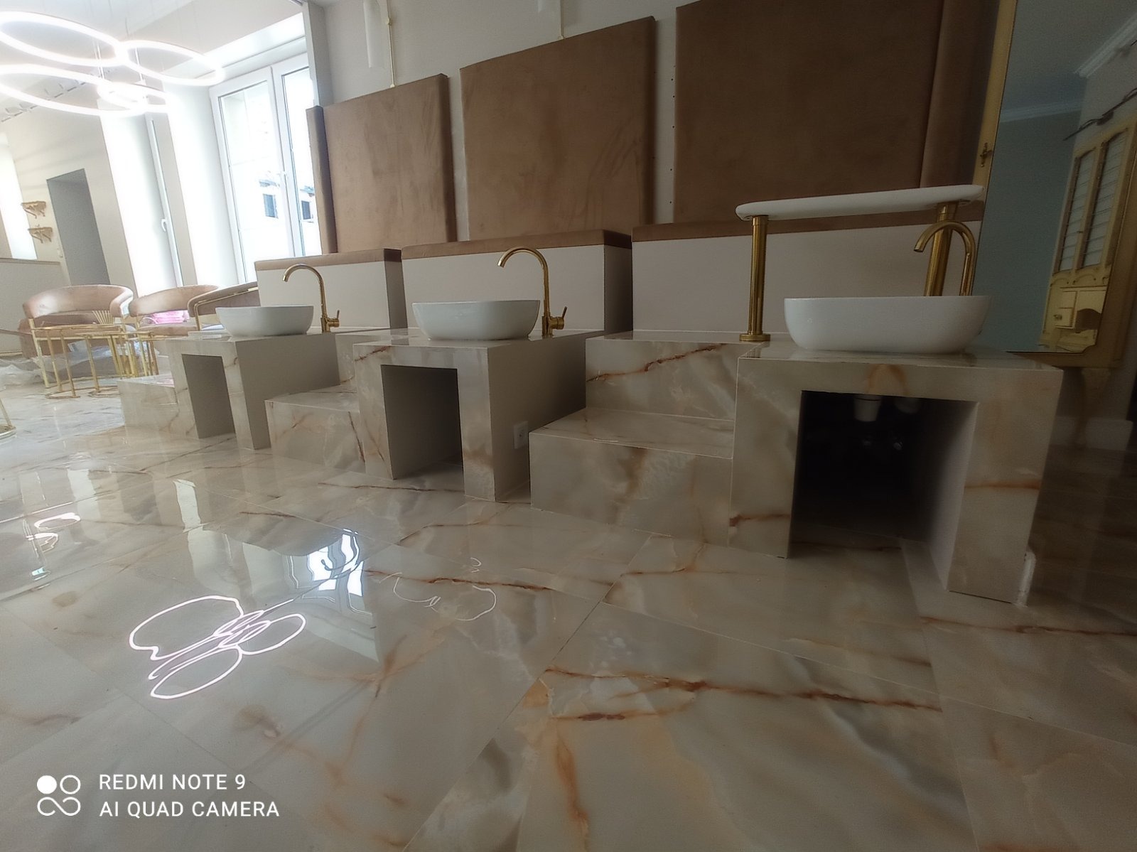 Luksusowe umywalki z marmuru z złotymi kranami w salonie kosmetycznym. Nowoczesny design z beżowymi panelami ściennymi i błyszczącą podłogą.