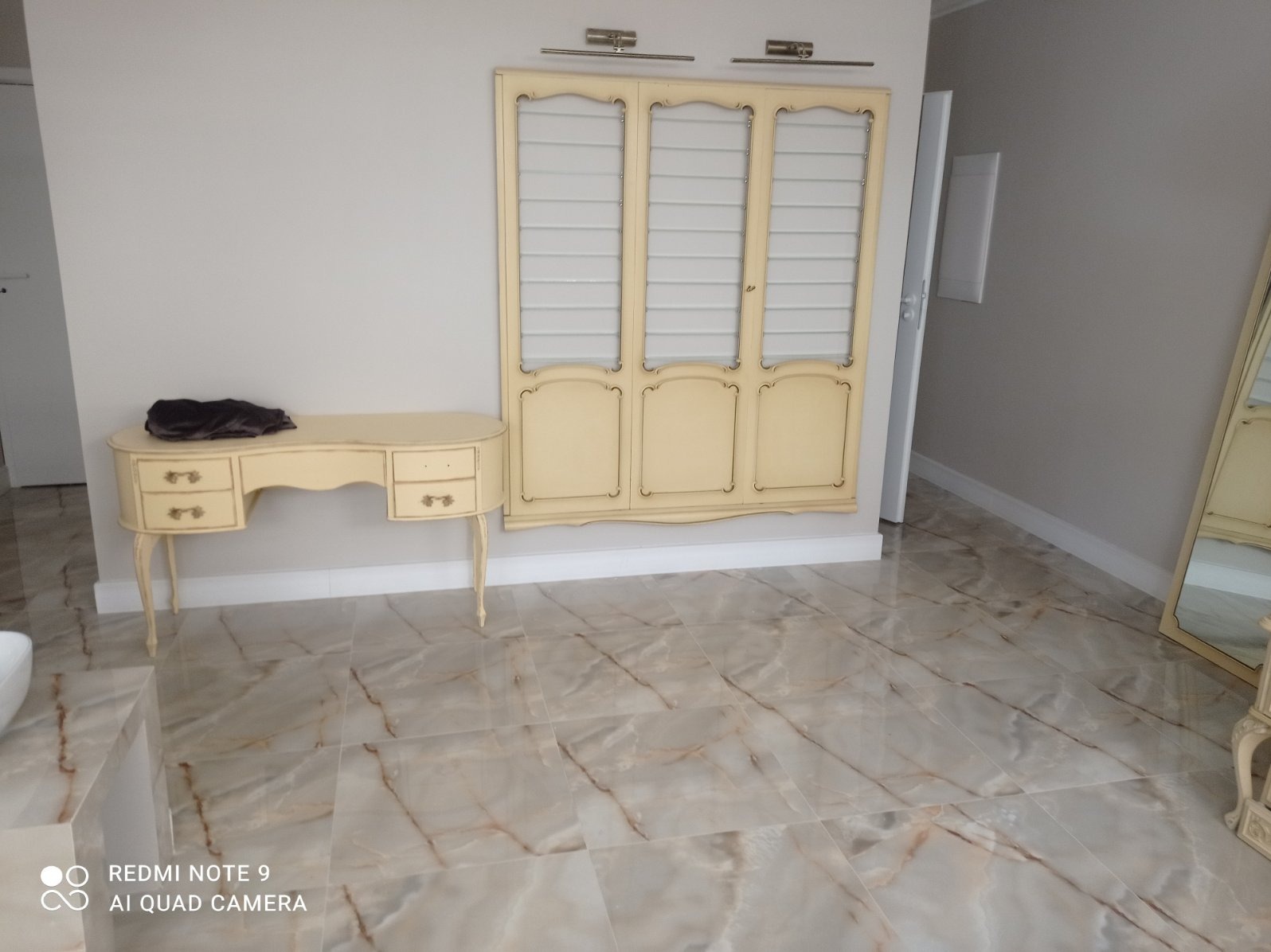 Jasne, marmurowe płytki podłogowe z kremowym biurkiem i szafką w stylu vintage. Widoczne detale wykończenia wnętrza i oświetlenie.