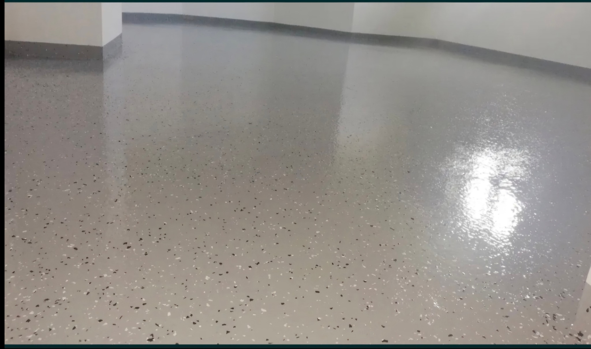 Błyszcząca, szara posadzka żywiczna z czarnymi i białymi elementami dekoracyjnymi w pomieszczeniu. Realizacja w Piekielniku.