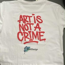 iWallDesign Kamil Musioł - Biała koszulka z czerwonym napisem 'Art is not a crime' i logo 'iWallDesign', leżąca na szarym tle. Widoczna metka. Nietypowa czcionka i układ.