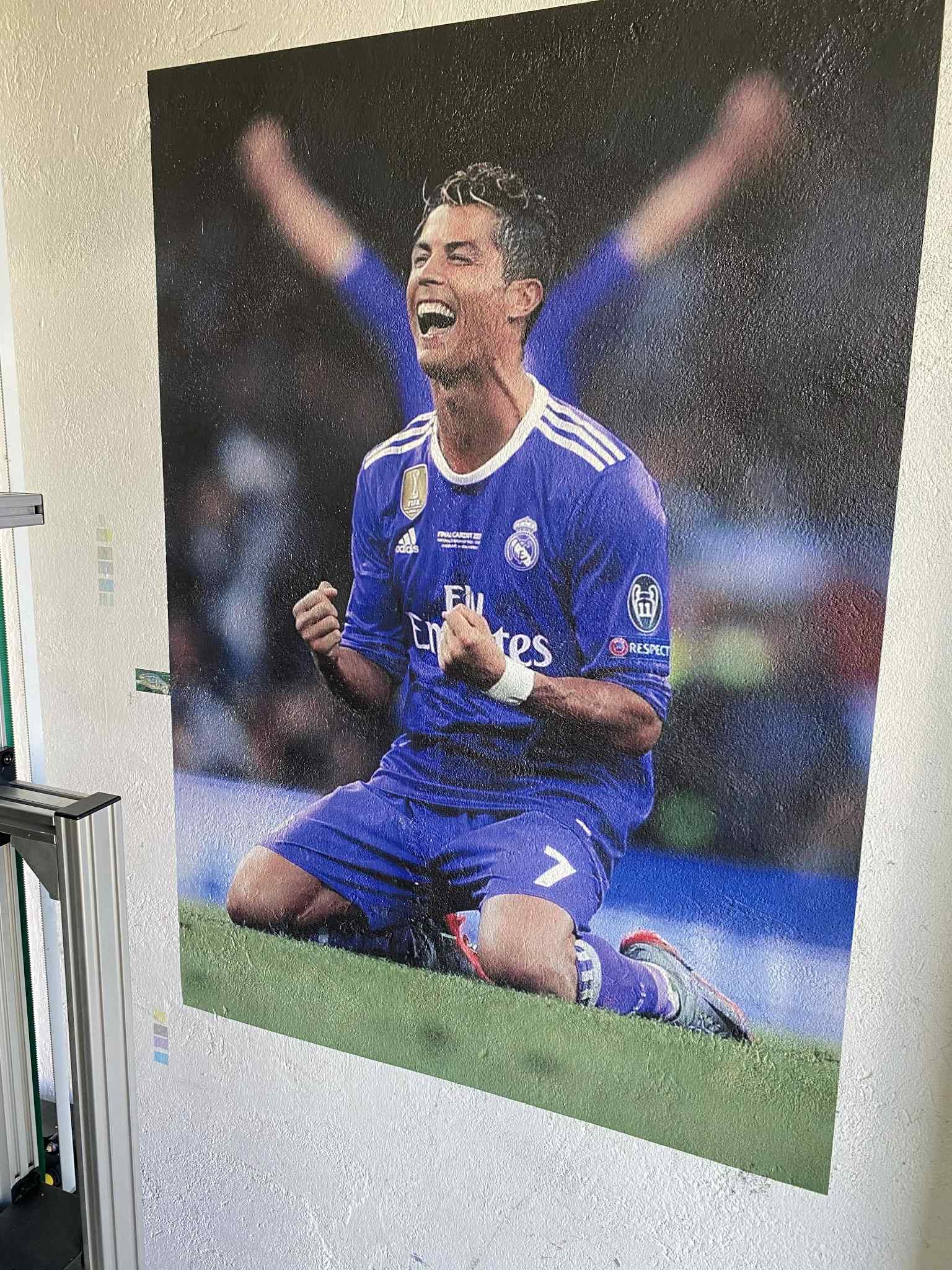 Duży format: wydruk portretu piłkarza w koszulce Realu Madryt na płótnie, widoczny fragment maszyny drukarskiej z boku. Intensywne kolory, żywe emocje.