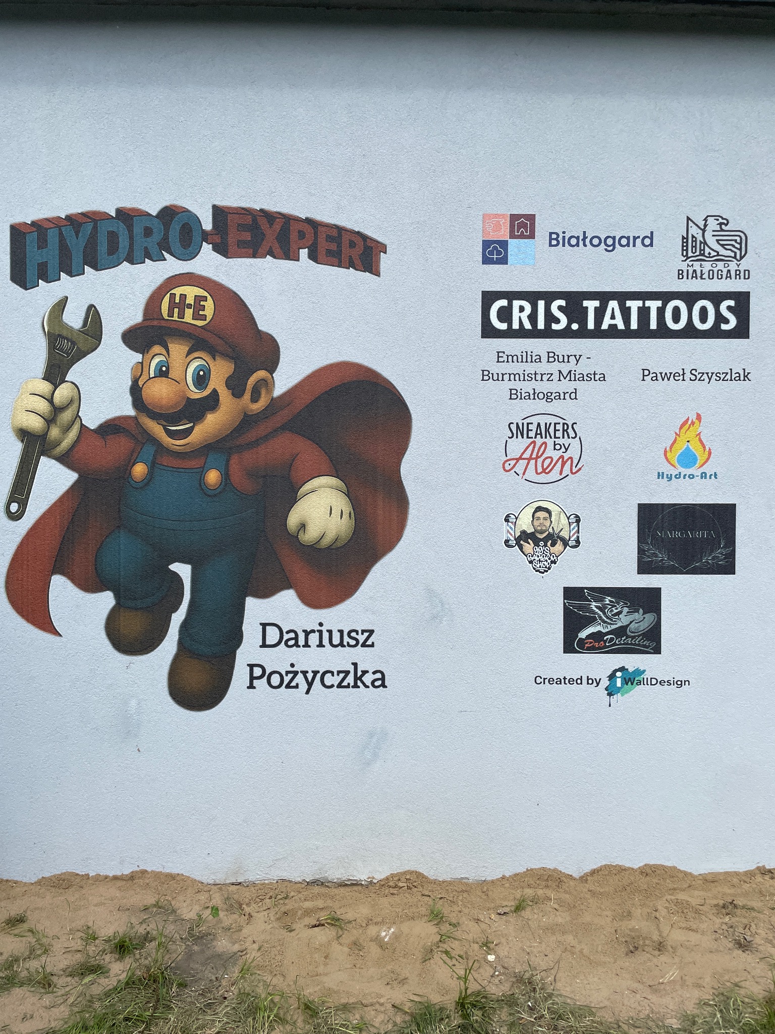 Mural reklamowy na ścianie budynku z postacią hydraulika w stylu Mario, logotypami firm i napisem 'Dariusz Pożyczka'.