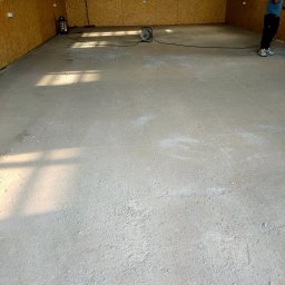 Kazare Quality Krzysztof Zaremba - Wnętrze w trakcie wykończenia: surowy beton na podłodze, ściany z płyt OSB, widoczny odkurzacz przemysłowy i zwinięty kabel.