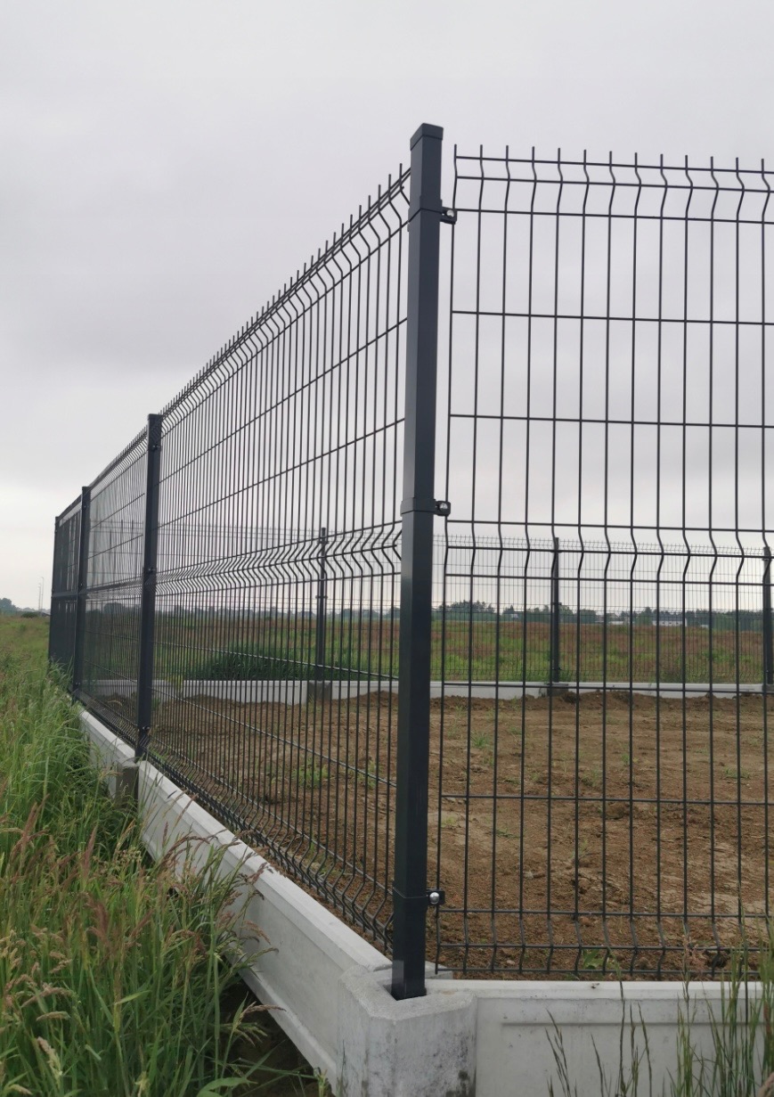 Nowoczesne ogrodzenie panelowe z podmurówką betonową na tle zieleni i pochmurnego nieba. Widoczne mocowania paneli do słupków.