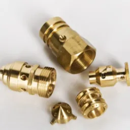 Precyzyjne, mosiężne elementy z gwintami, różnej wielkości i kształtu, leżące na białym tle. Widoczne detale obróbki, otwory i gwinty.