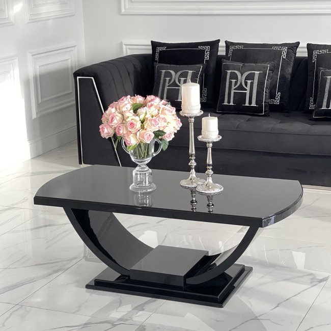 Elegancki, czarny stolik kawowy w wysokim połysku z dekoracjami (świece, kwiaty) na tle czarnej sofy z ozdobnymi poduszkami. Styl glamour.