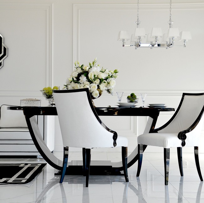 Elegancki stół jadalniany w stylu art déco z czarnym, lakierowanym blatem i białymi krzesłami. Na stole wazon z białymi kwiatami. Całość w jasnym, nowoczesnym wnętrzu.