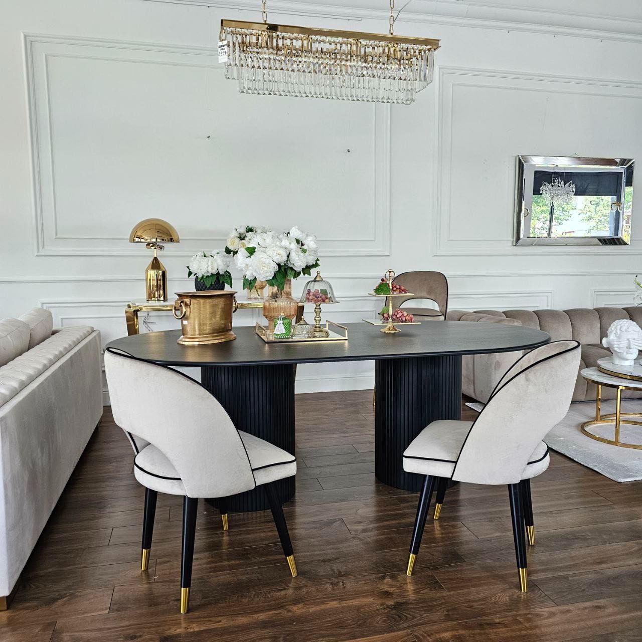 Eleganckie, beżowe krzesło tapicerowane z czarną lamówką i złotymi akcentami na nogach, ustawione przy owalnym, czarnym stole w stylowym wnętrzu.