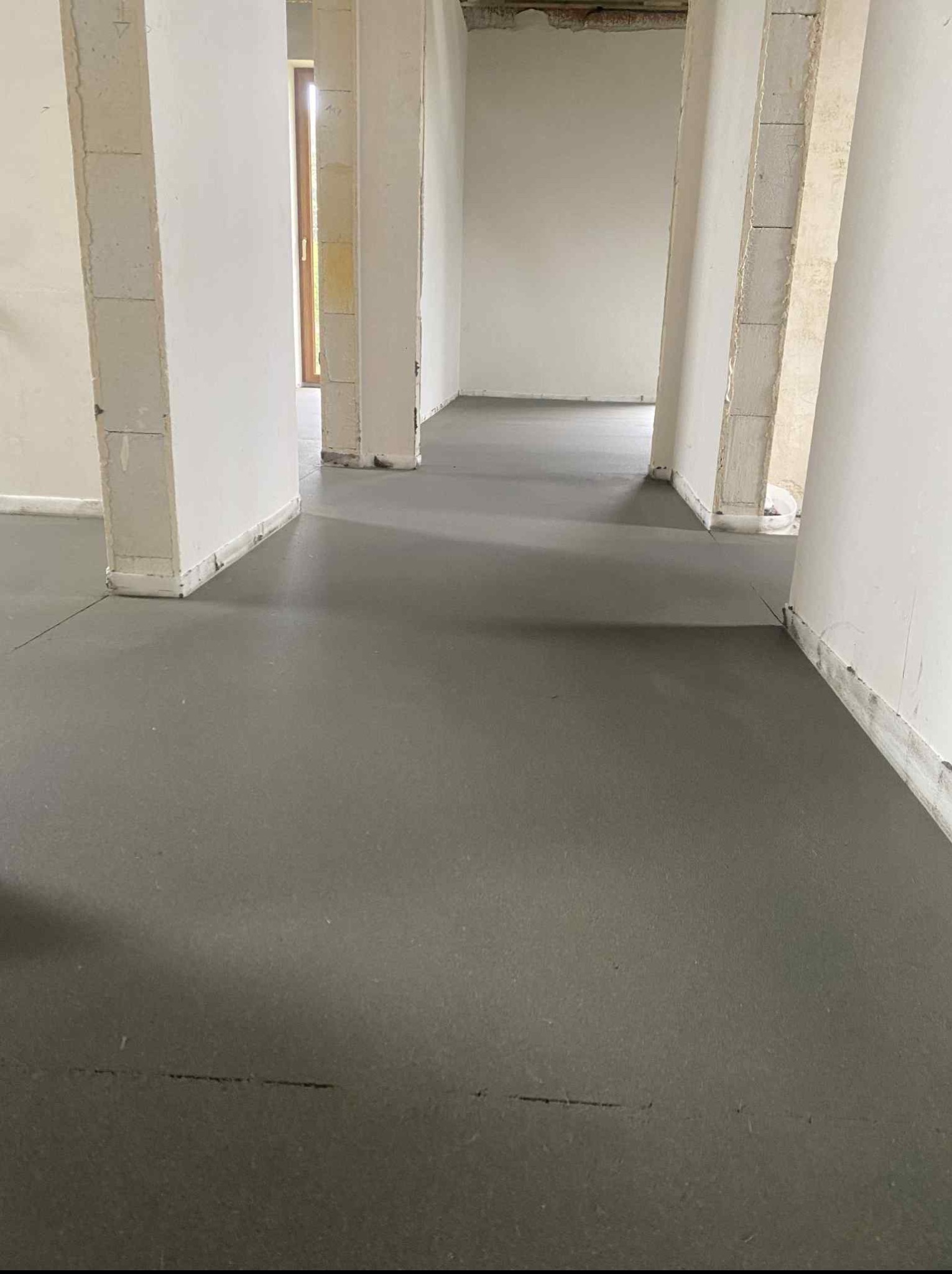 Świeżo wylana, gładka posadzka jastrychowa w surowym wnętrzu z białymi ścianami i widocznymi fragmentami konstrukcji. Minimalistyczny, surowy styl wykończenia.