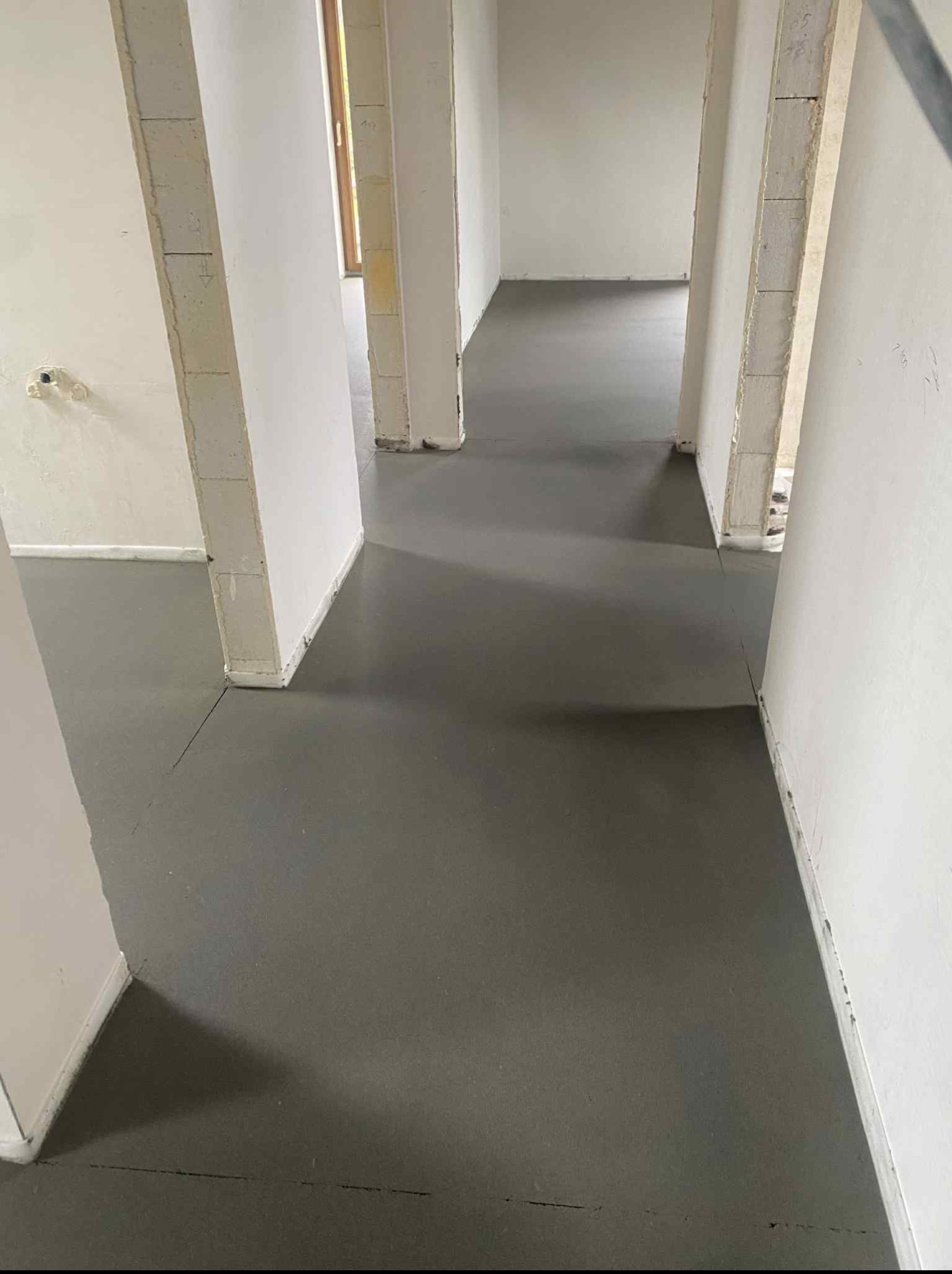 Świeżo wylana, gładka posadzka jastrychowa w surowym wnętrzu z widocznymi blokami ścian i otworami drzwiowymi. Długie, proste pęknięcie na powierzchni posadzki.