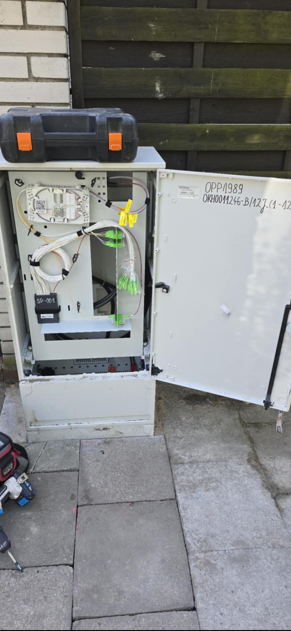 Otwarta szafka telekomunikacyjna z kablami światłowodowymi i narzędziami obok, na zewnątrz budynku w Stargardzie. Widoczna skrzynka narzędziowa.