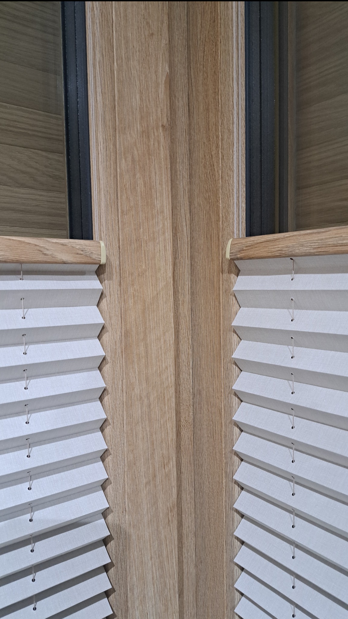 Zamknięte, białe plisy okienne na drewnianej ramie okiennej. Widoczne detale plisowania i sznurki. Ujęcie z bliska, podkreślające strukturę materiału i precyzję montażu.