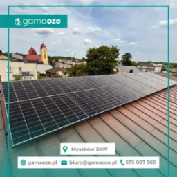 Panele fotowoltaiczne na dachu domu w Myszkowie, z widokiem na kościół w tle. Instalacja solarna z logo firmy Gamaoze.pl.