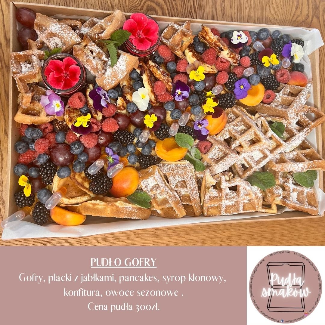 Pudełko gofrów z owocami sezonowymi, plackami jabłkowymi i pancakes, posypane cukrem pudrem, udekorowane jadalnymi kwiatami.