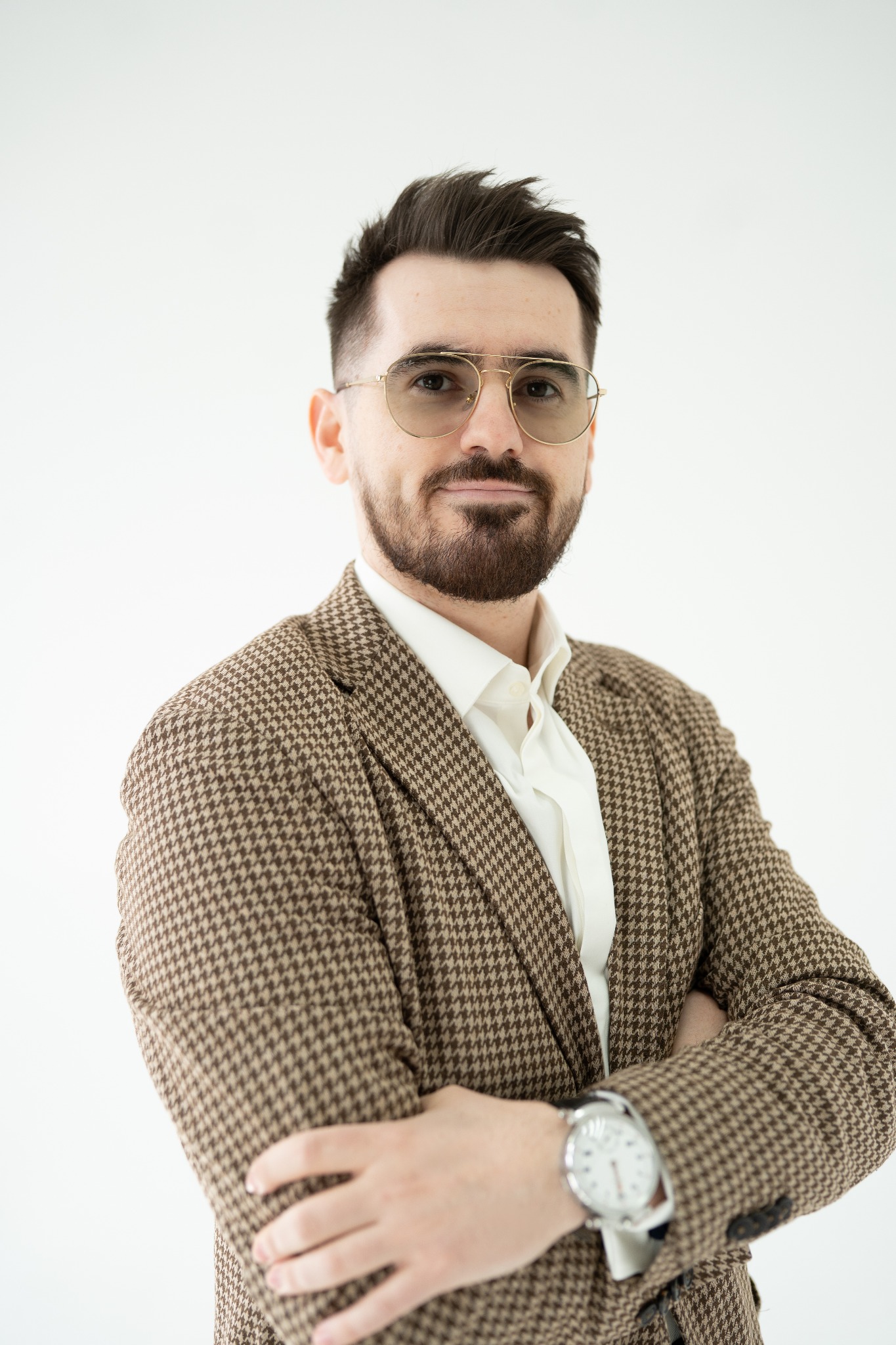 Portret mężczyzny w brązowej marynarce w pepitkę i okularach, z zegarkiem na ręce, na jasnym tle. Profesjonalny wizerunek.