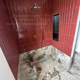 Masterscraft Renovations sp z o.o - Nowoczesna kabina prysznicowa z bordowymi, podłużnymi płytkami i kamienną posadzką. Widoczna deszczownica i wnęka w ścianie.