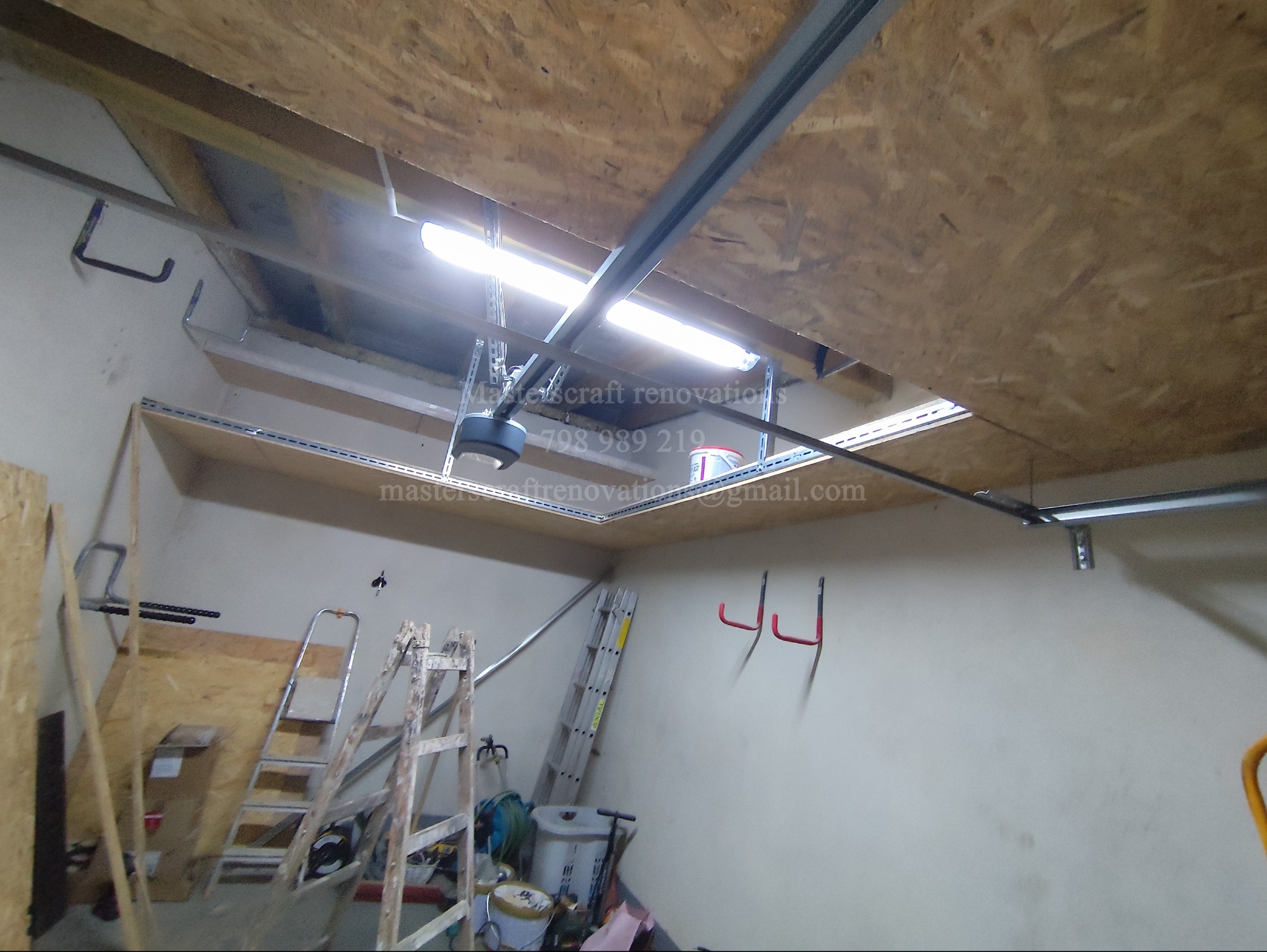 Wykończone wnętrze garażu z oświetleniem LED i konstrukcją sufitową, widok z dołu, drabiny i narzędzia w tle. Jasne, robocze światło.