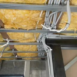 Sufit podwieszany z izolacją z wełny mineralnej i równolegle ułożonymi, szarymi peszlami elektrycznymi, przymocowanymi do metalowych profili.