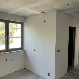 Grupa MFC sp. z o.o. - Nowe mieszkanie w stanie deweloperskim: widok na wnętrze z oknem, widoczne otwory na gniazdka, sufit podwieszany z otworami na oświetlenie.