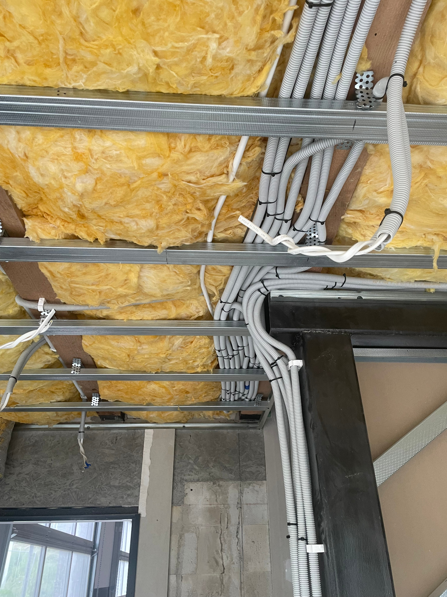 Sufit podwieszany z izolacją z wełny mineralnej i równolegle ułożonymi, szarymi peszlami elektrycznymi, przymocowanymi do metalowych profili.