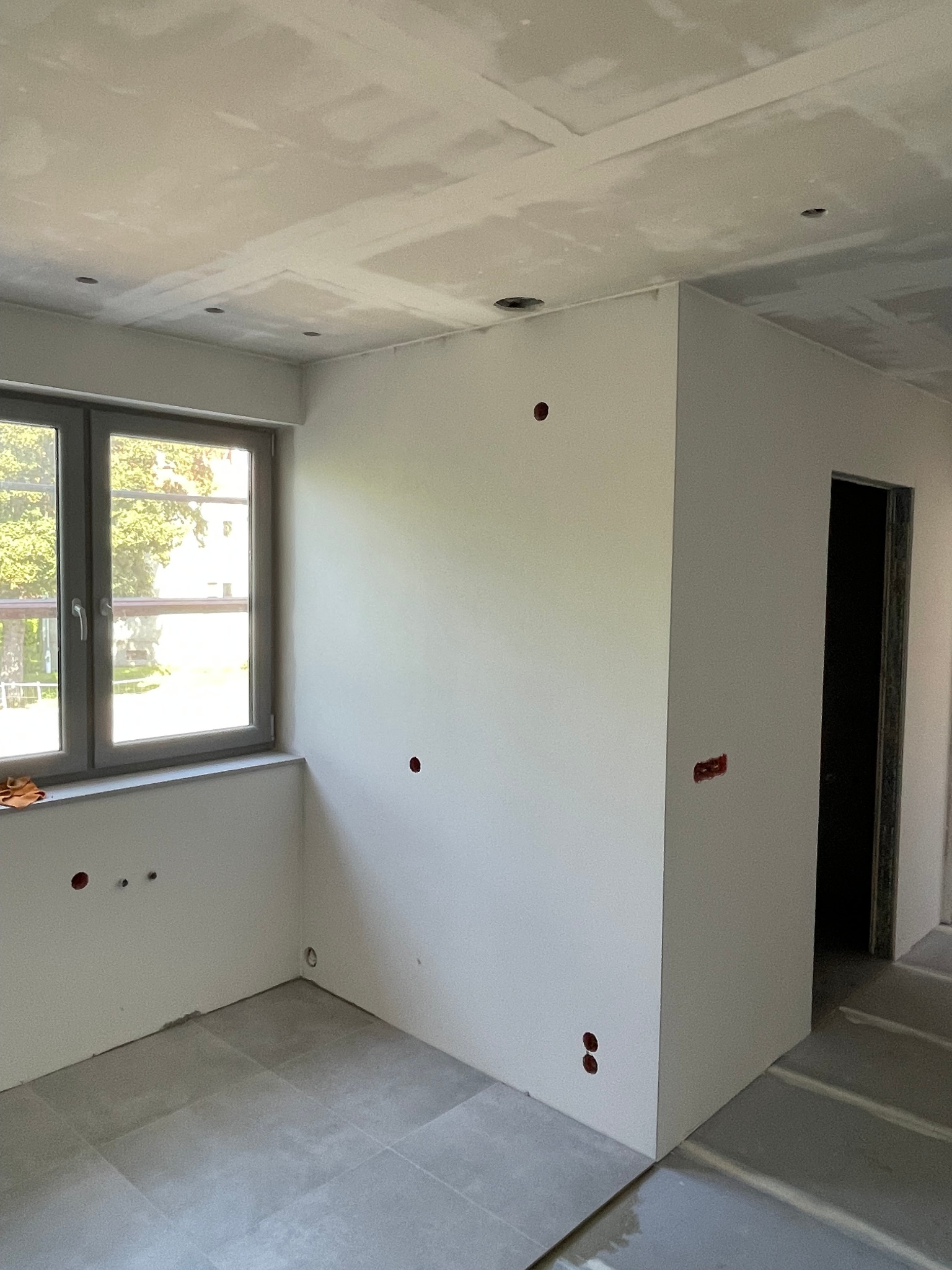 Nowe mieszkanie w stanie deweloperskim: widok na wnętrze z oknem, widoczne otwory na gniazdka, sufit podwieszany z otworami na oświetlenie.