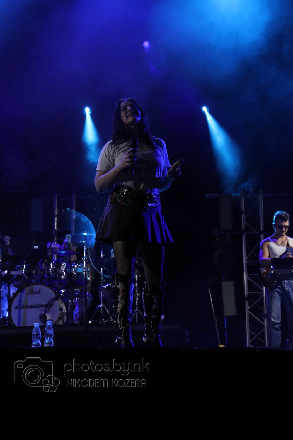 Fotografia eventowa z Wierzbicy: wokalistka na scenie, oświetlona reflektorami, w tle zespół muzyczny i perkusja. Ujęcie z dołu, dynamiczne.