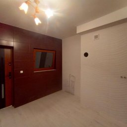 Tomasz M - Wnętrze po remoncie: brązowe płytki na ścianie z drzwiami i oknem, biała ściana z dekoracyjną fakturą. Widoczne rury instalacji i designerska lampa sufitowa.
